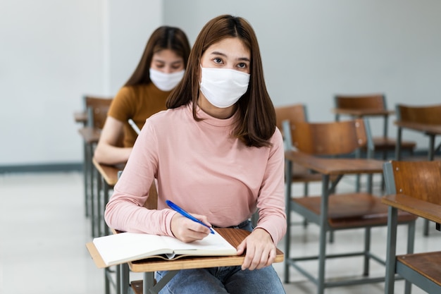 Grupo de estudantes universitários usando máscara facial e mantendo distância enquanto estudam na sala de aula e no campus da faculdade ou universidade para prevenir a pandemia de COVID-19. A nova vida no campus da faculdade ou universidade