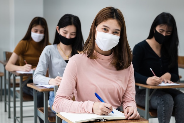 Grupo de estudantes universitários usando máscara facial e mantendo distância enquanto estudam na sala de aula e no campus da faculdade ou universidade para prevenir a pandemia de COVID-19. A nova vida no campus da faculdade ou universidade