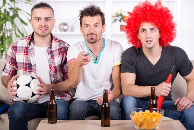 Grupo de fãs de esportes estão assistindo jogo na TV em casa.