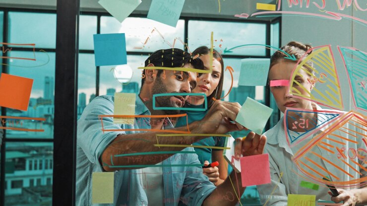 Foto grupo de feliz equipe de negócios profissionais trabalhando juntos discutindo e escrevendo em notas adesivas sobre estratégia de plano de ideia de marketing em parede de vidro com gráfico e notas adesivas coloridas tracery.