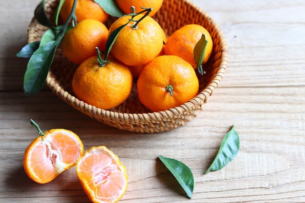 Grupo de frutas frescas de tangerina com folhas na cesta de vime na mesa de madeira