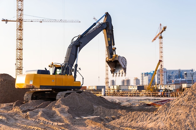 Grupo de guindastes de torre e silhueta de escavadeira no canteiro de obras, a superfície do céu ao pôr do sol.