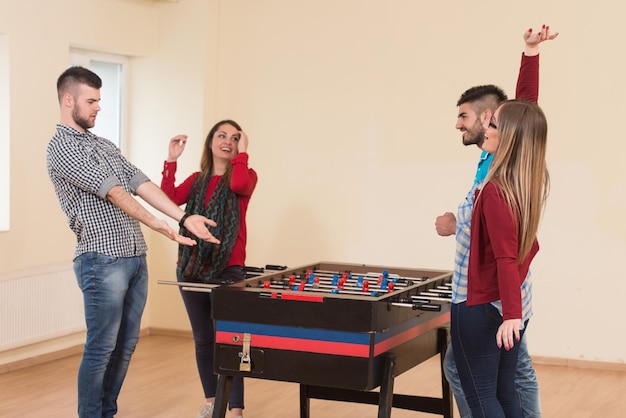 Grupo de homens e mulheres jovens desfrutando de um jogo de pebolim