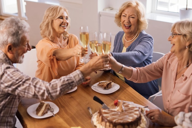 Grupo de idosos alegres levantando um copo e brindando em uma festa de aniversário em casa