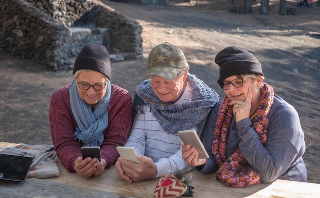 Grupo de idosos maduros sorridentes olhando para o celular Sentado em uma mesa de madeira na área de piquenique da montanha desfrutando de uma caminhada ao ar livre Conceito de tecnologia e comunicação global
