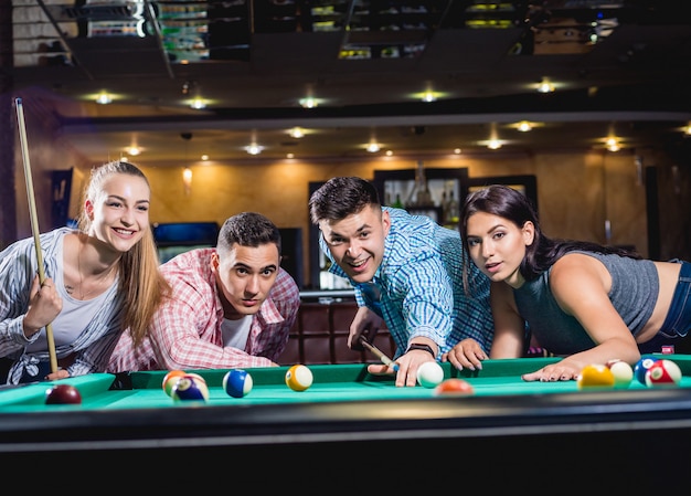 Grupo de jovens amigos alegres jogando bilhar.