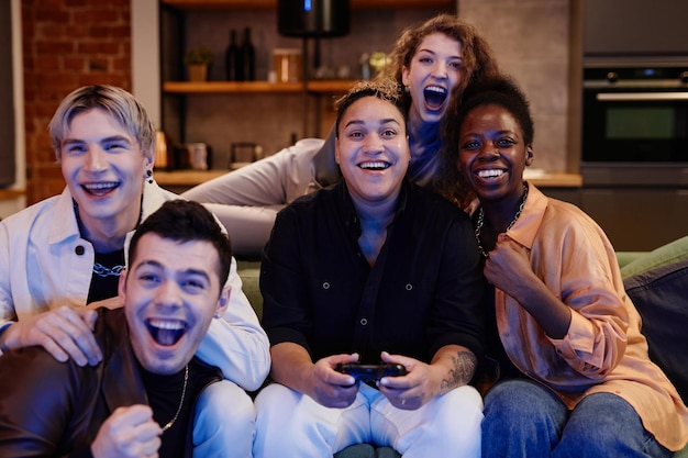 Grupo de jovens amigos animados interculturais sentados em frente ao aparelho de tv e jogando videogame para obter
