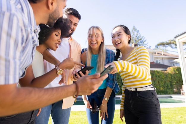 Grupo de jovens amigos diversos ao ar livre rindo e olhando para o smartphone juntos