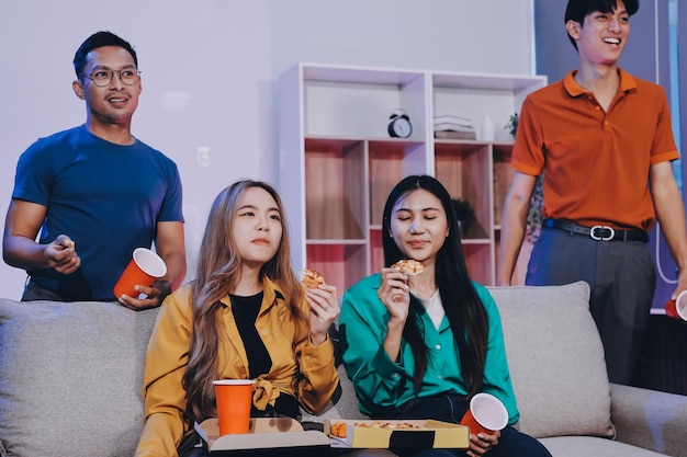 Grupo de jovens amigos felizes almoçando em casa festa familiar na Ásia comendo pizza e rindo desfrutando da refeição enquanto estão sentados juntos na mesa de jantar em casa celebração de férias e união