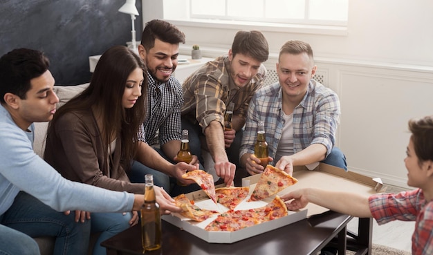Grupo de jovens amigos multiétnicos com pizza e garrafas de bebida comemorando em casa