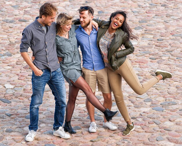 Grupo de jovens amigos sorridentes tentando levantar e mover as pernas simultaneamente como uma divertida atividade de união Conceito