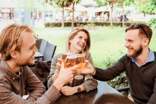 Grupo de jovens amigos sorridentes tocando copos de cerveja em um café de rua como um conceito de amizade e união