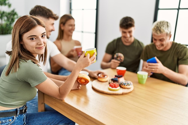 Grupo de jovens amigos sorrindo feliz tomando café da manhã sentado na mesa em casa.
