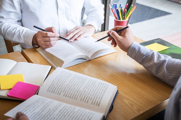 Grupo de jovens aprendendo a estudar nova lição para o conhecimento na biblioteca durante o ensino da educação de amigos na preparação para o exame