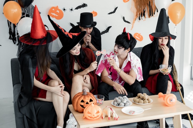 Grupo de jovens asiáticos fantasiados de bruxa, mago, inferno, comemorar festa na sala para o tema Halloween em casa. Gang teen tailandês com festa de Halloween com sorriso. Conceito de festa de Halloween em casa.