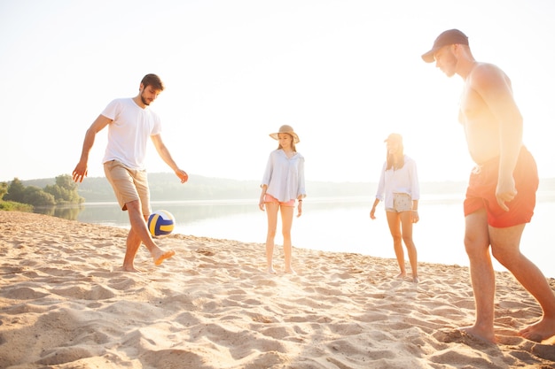 Grupo de jovens brincando com bola na praia. jovens amigos curtindo as férias de verão em uma praia arenosa.