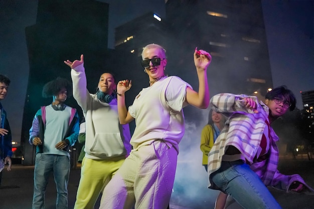 Grupo de jovens dançando na rua à noite com roupas modernas e luzes coloridas