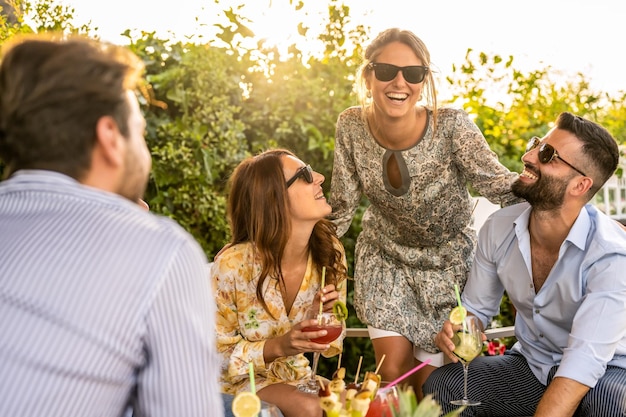 Grupo de jovens de 30 anos se divertindo em um coquetel ao ar livre belas mulheres sorrindo e rindo com amigos homens bonitos conversando com elegantes millenials femininos