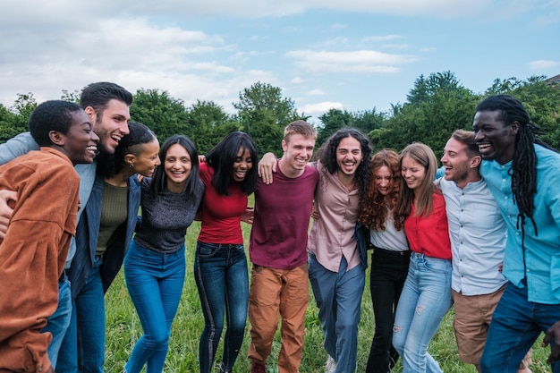 Grupo de jovens de origem multiétnica juntos abraçando e se divertindo ao ar livre