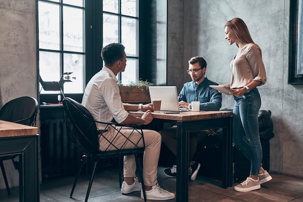 Grupo de jovens em roupas casuais inteligentes, usando tecnologias modernas, enquanto trabalham no escritório