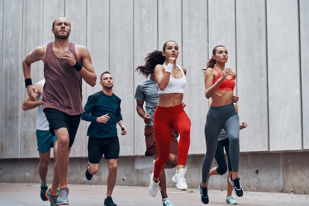 Grupo de jovens em roupas esportivas correndo enquanto se exercitam ao ar livre