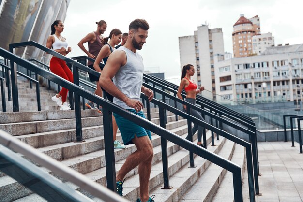 Grupo de jovens em roupas esportivas correndo enquanto se exercitam nas escadas ao ar livre