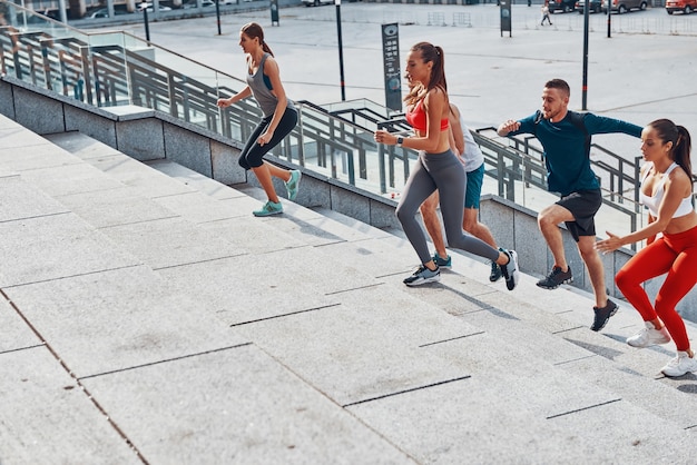 Grupo de jovens em roupas esportivas correndo enquanto se exercitam nas escadas ao ar livre