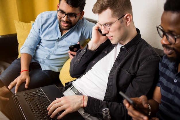 Grupo de jovens empreendedores em busca de ideias de negócios, usando laptop e smartphones, trabalhando juntos em um projeto, falando ao telefone. alunos multiétnicos em busca de trabalho navegando na internet.