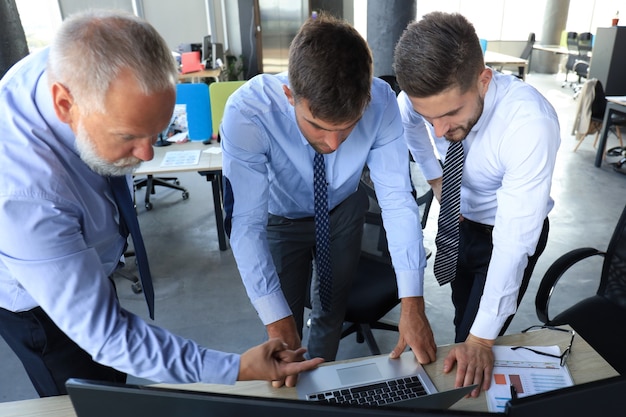 Grupo de jovens empresários em trajes formais, trabalhando usando computadores enquanto está sentado no escritório.