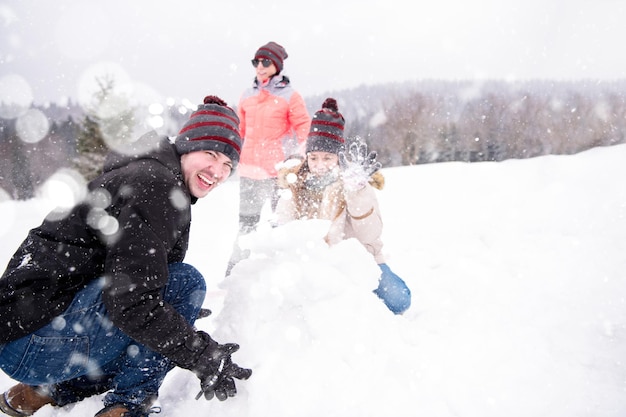 grupo de jovens empresários felizes tendo uma competição em fazer bonecos de neve enquanto aproveita o dia de inverno nevado com flocos de neve ao redor deles durante uma formação de equipe na floresta de montanha
