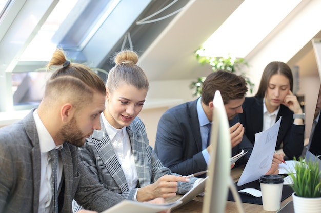 Grupo de jovens empresários trabalhando, comunicando-se enquanto está sentado na mesa do escritório junto com os colegas.