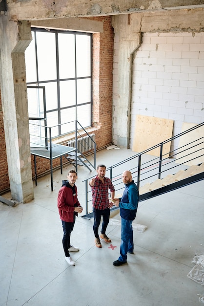 Grupo de jovens engenheiros ou empreiteiros em pé na escada enquanto discutem a qualidade do trabalho dos construtores em construções inacabadas