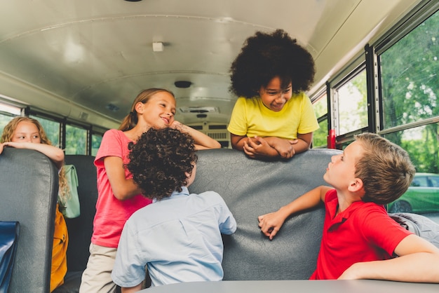 Foto grupo de jovens estudantes que frequentam a escola primária em um ônibus escolar amarelo - crianças do ensino fundamental se divertindo