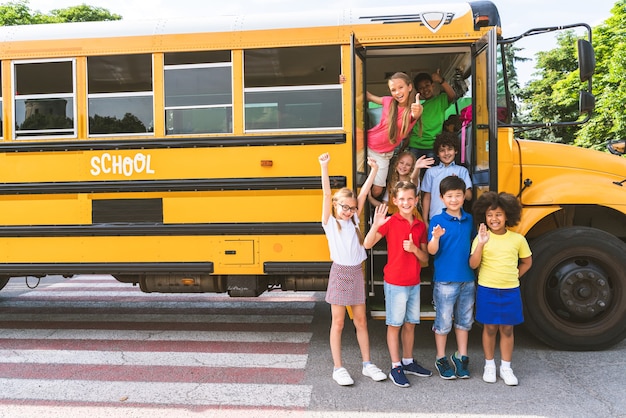 Foto grupo de jovens estudantes que frequentam a escola primária em um ônibus escolar amarelo - crianças do ensino fundamental se divertindo