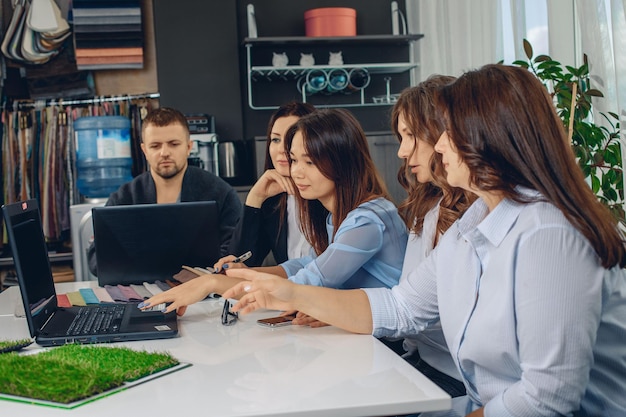 Grupo de jovens experientes e promissores trabalhadores de escritório ambiciosos, sentados no escritório em uma mesa branca e discutindo sobre como olhar para um laptop no escritório de criatividade. Conceito de produtividade