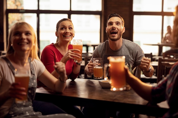 Grupo de jovens felizes bebendo cerveja e assistindo jogo esportivo na TV em um pub