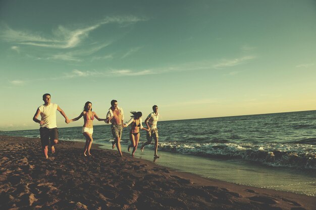 grupo de jovens felizes se divertem correndo e pulando em beacz na hora do pôr do sol