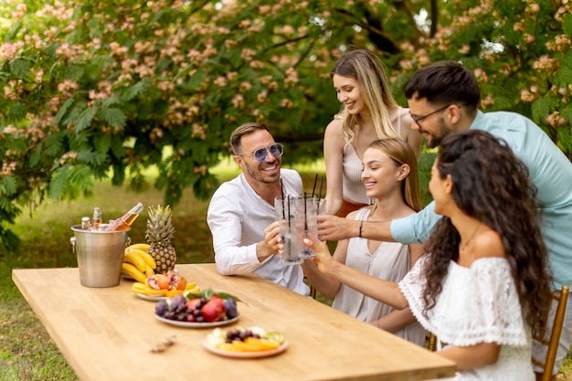 Grupo de jovens felizes torcendo com limonada fresca e comendo frutas no jardim