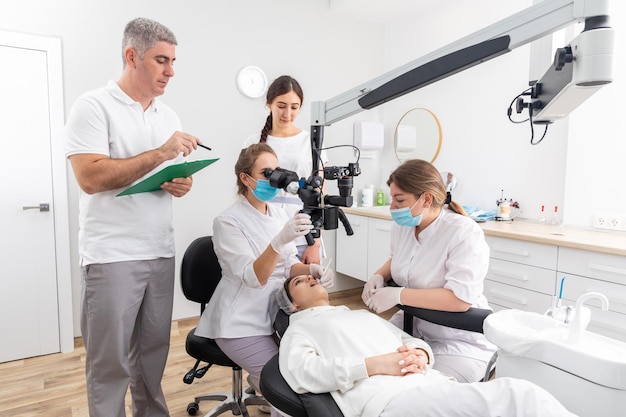 Grupo de jovens médicos aprendendo na clínica odontológica assistindo tratamento odontológico com microscópio