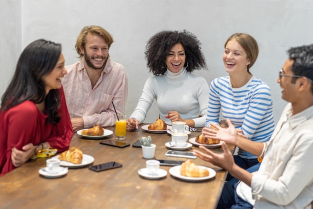 Foto grupo de jovens millennials tomando café da manhã trabalhando em um momento de pausa croissants e bolos café e cappuccino na mesa de um bar