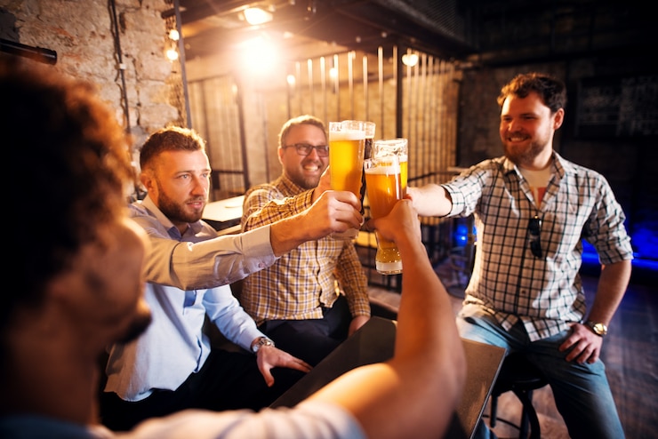 Foto grupo de jovens positivos, brindando com uma cerveja no ensolarado pub depois do trabalho.