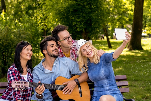 Grupo de jovens tirando uma selfie e tocando violão enquanto se divertem no parque