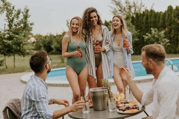 Grupo de jovens torcendo com bebidas e comendo frutas à beira da piscina no jardim