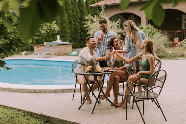 Grupo de jovens torcendo com cidra à beira da piscina no jardim