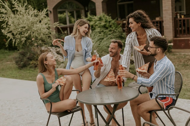 Grupo de jovens torcendo com cidra e comendo pizza à beira da piscina no jardim