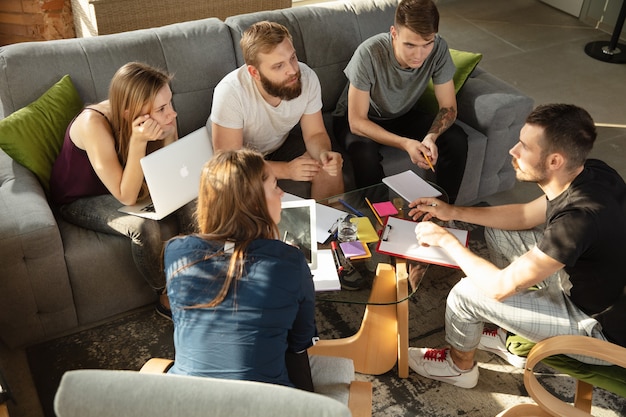 Grupo de jovens trabalhadores de escritório caucasianos se reunindo para discutir novas idéias. Reunião criativa. Trabalho em equipe e brainstorming. Homens e mulheres se reúnem no cargo para planejar seu trabalho futuro. Conceito de negócios.