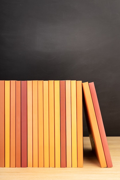 Grupo de livros laranja na mesa de madeira ou prateleiras e quadro-negro no fundo. Copie o espaço
