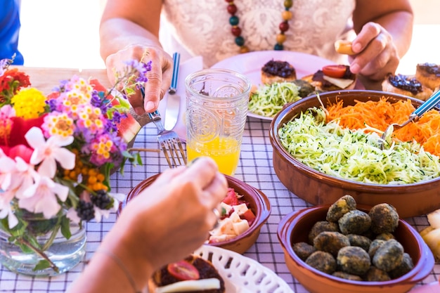 Grupo de mãos compartilhando comida e bebida Povos caucasianos desfrutando de brunch ou refeição juntos Frutas e legumes na mesa de madeira Luz do sol ao ar livre no terraço