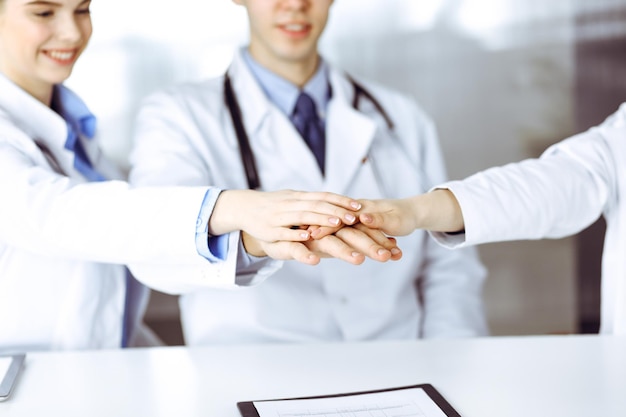 Grupo de médicos juntando as mãos como um círculo e pronto para ajudar os pacientes enquanto está sentado na mesa no escritório do hospital moderno. Trabalho em equipe bem-sucedido em medicina, conceito de combate ao Coronavirus