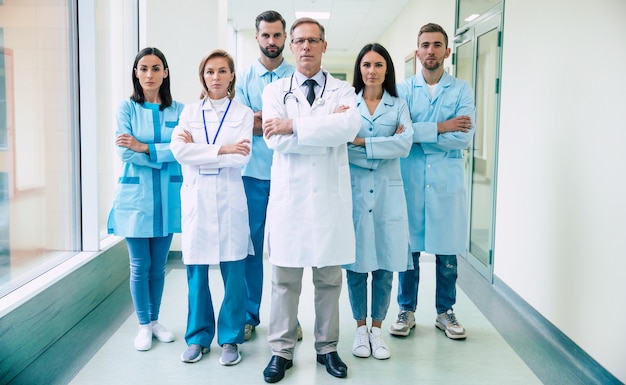 Grupo de médicos modernos bem-sucedidos e confiantes posando e olhando para a câmera no corredor do hospital